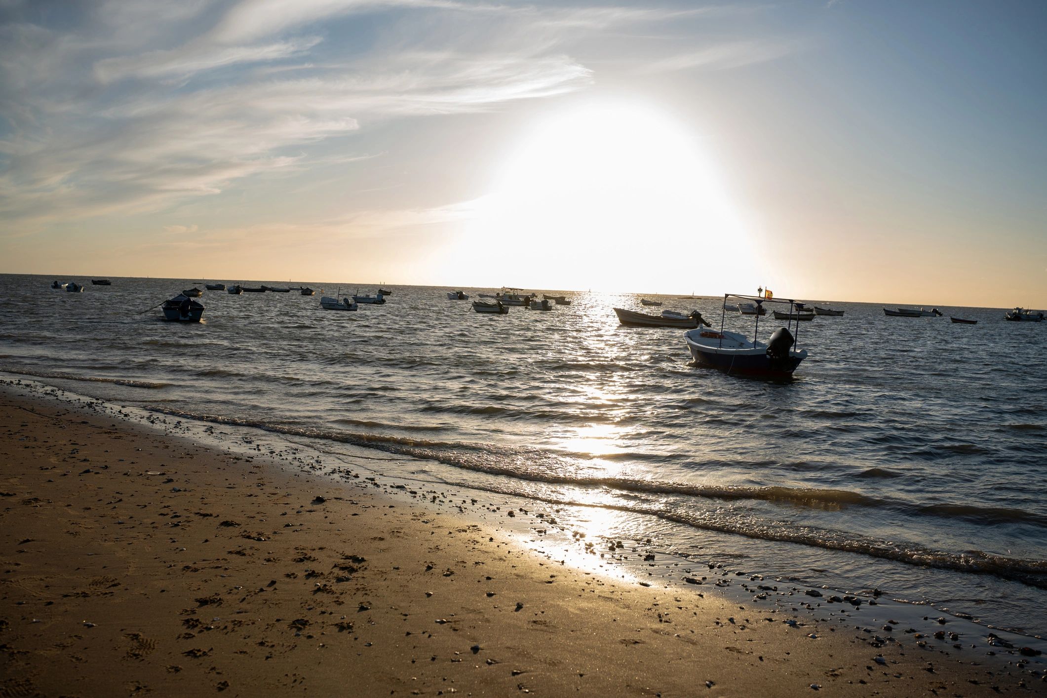 Boats anchored on the water near a sandy beach at sunset